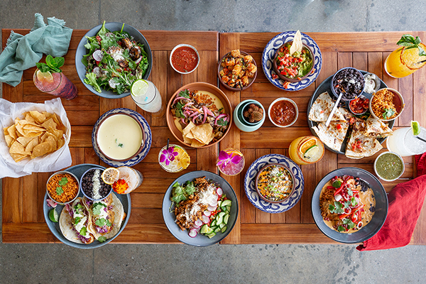 Overhead shot of a table full of salsas, tacos, sides, cocktails, and more from Gezzo's West Coast Burritos.