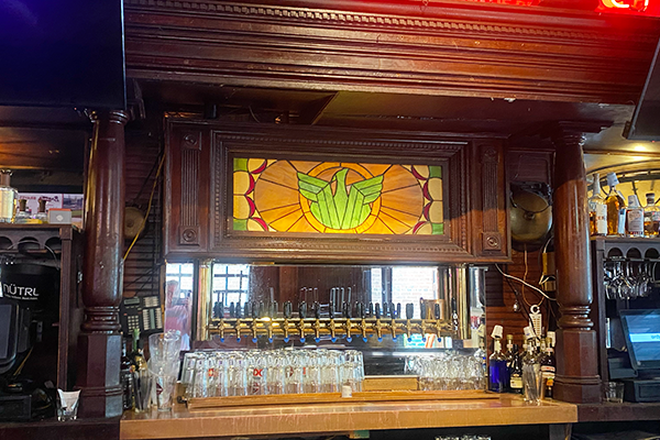 A green and orange stained glass portrait of a phoenix behind a bar