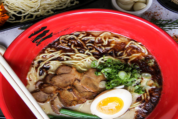 A red bowl containing ramen with meat, noodles, and ramen broth