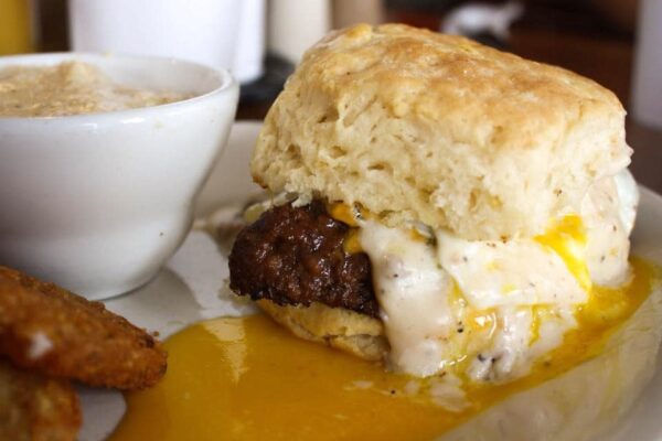 A biscuit sandwich with sausage and a runny egg with a side of grits