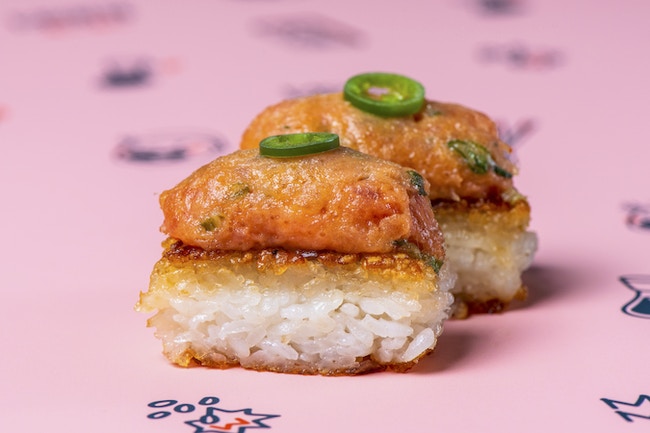 A fried square of rice topped with spicy tuna and a slice of jalapeno