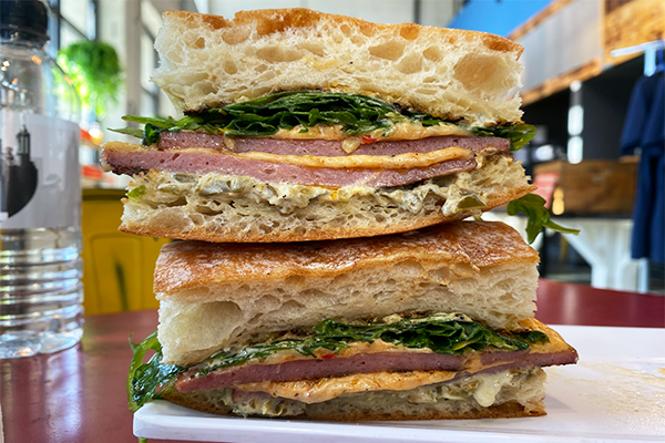 Two sandwich halves stacked on top of each other, topped with bologna, pimento cheese, aioli, and dressed arugula