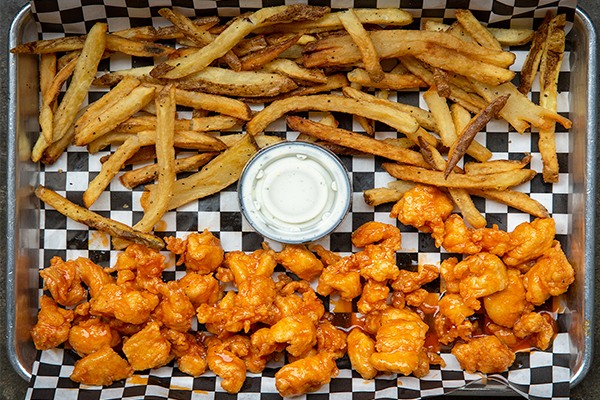 Fried pieces of chicken and french fries on a checkered paper with a cup of ranch in the middle