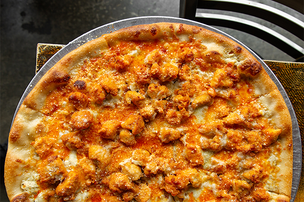 Buffalo chicken pizza on a silver tray on a brown table 