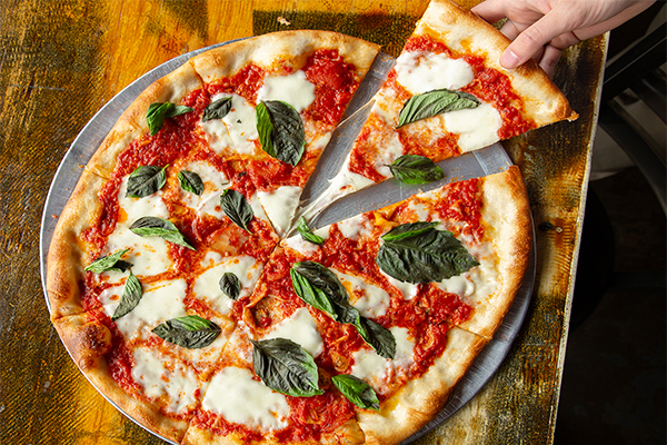 Pizza with white mozzarella, green basil, and red sauce. A slice is being pulled from the pie