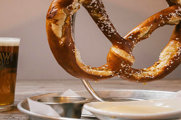 Large pretzel with beer cheese and mustard in the foreground and a glass of beer on the left